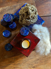 Blue glittery lidded amber jars on a wooden surface with a small painting below. 