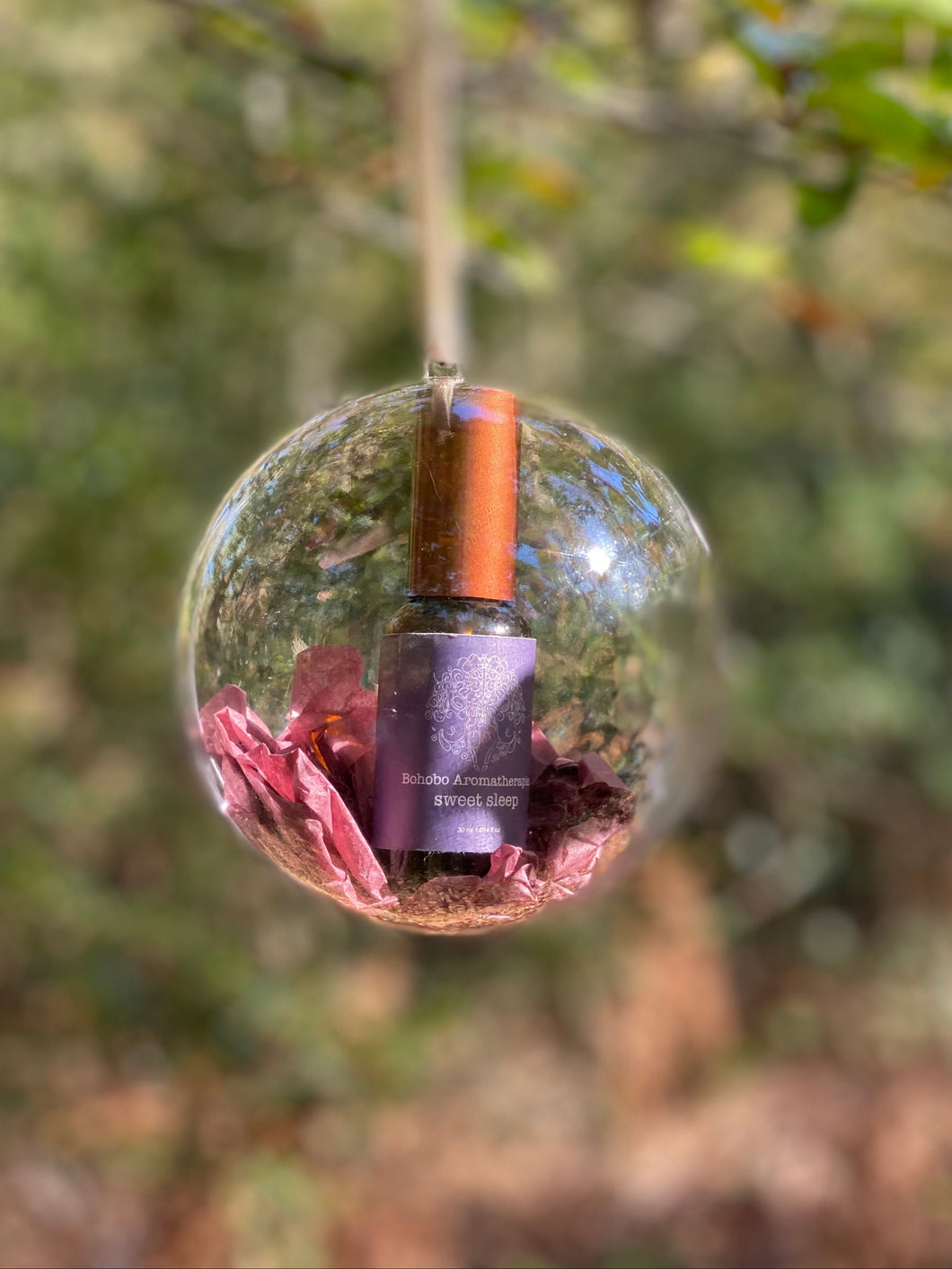 Glass sphere with a bottle inside, surrounded by flowers, against a natural background.