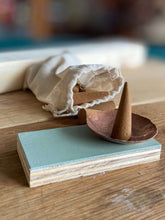 Small wooden incense holder with a cone on a light blue base, placed on a wooden surface.