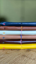 Stack of colorful leather notebooks on a wooden surface with a green background