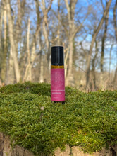Roll-on bottle with pink label on a mossy surface with trees in the background